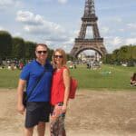 Ila and Gabriel posing for a photo in the Champs de Mars Gardens, Paris, with the entire Eiffel Tower visible.
