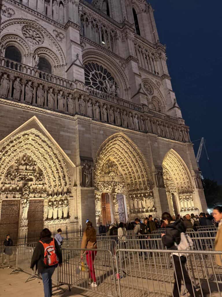 Notre Dame Cathedral in Paris illuminated at 6 PM (18:00) in autumn, with people visible in front, captured during Gabriel's evening walk.