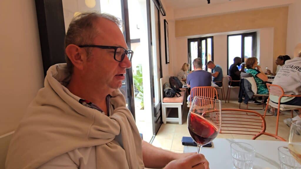 Gabriel, the travel companion, tasting a local Rhodian red wine in a Lindos restaurant, confirming the sensory journey and group's E-E-A-T.