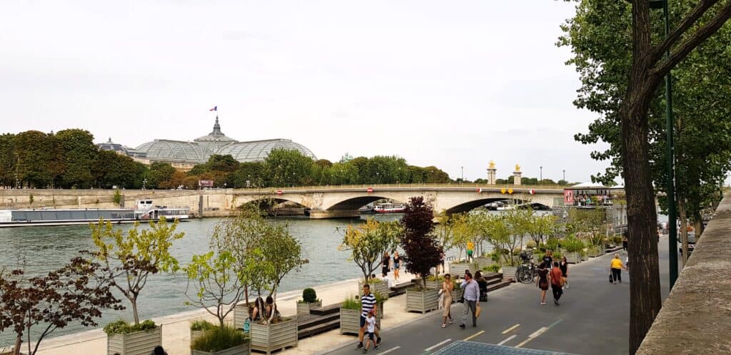 The Seine River banks in Paris, perfect for walking or scootering, featuring trees and people relaxing by the river.