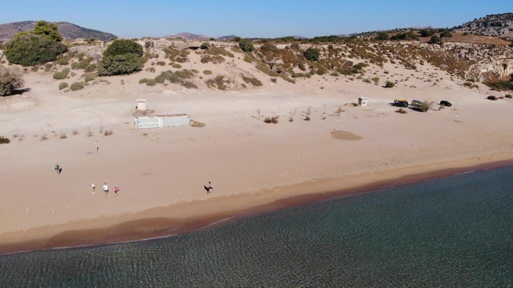 Panoramic view of Agathi Beach Rhodes, showing the free and ample unpaved dirt parking area right next to the golden sand.