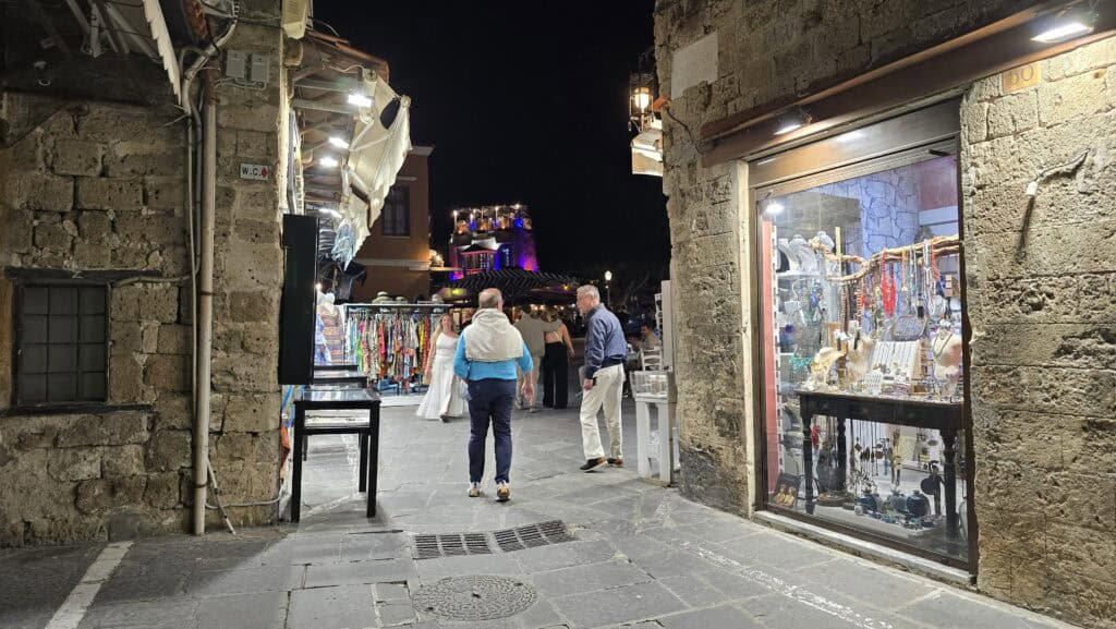 Gabriel walking through the illuminated Aristoteles Square (Platía Aristotélous) in Rhodes Old Town at night, showing the quiet, medieval atmosphere.