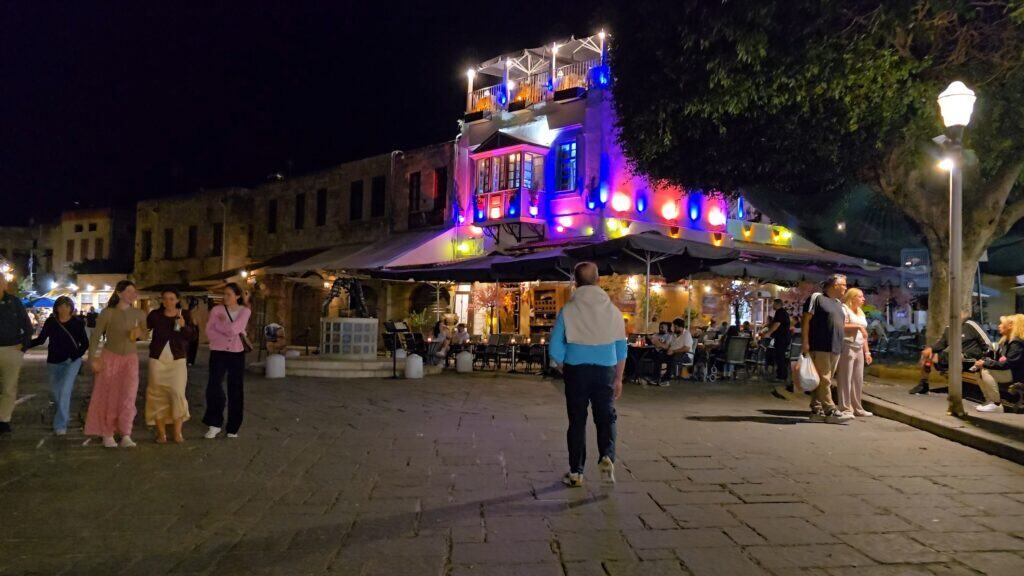 Highly colorful, brightly lit bar/restaurant near Aristotelous or Hippocrates Square, designed to attract tourists, with visible rooftop access.