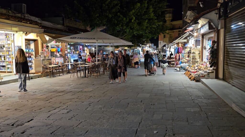 Night view of Sokratous Street (Sokratous 129) in Rhodes Old Town, showing a mix of open shops, closed stores, and evening bars.