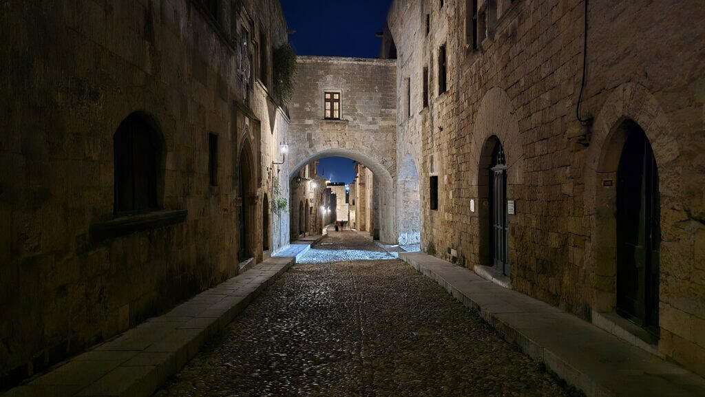 Night view of the virtually empty Street of the Knights (Odós Ippotón) in Rhodes Old Town, illuminated by antique-style lanterns.