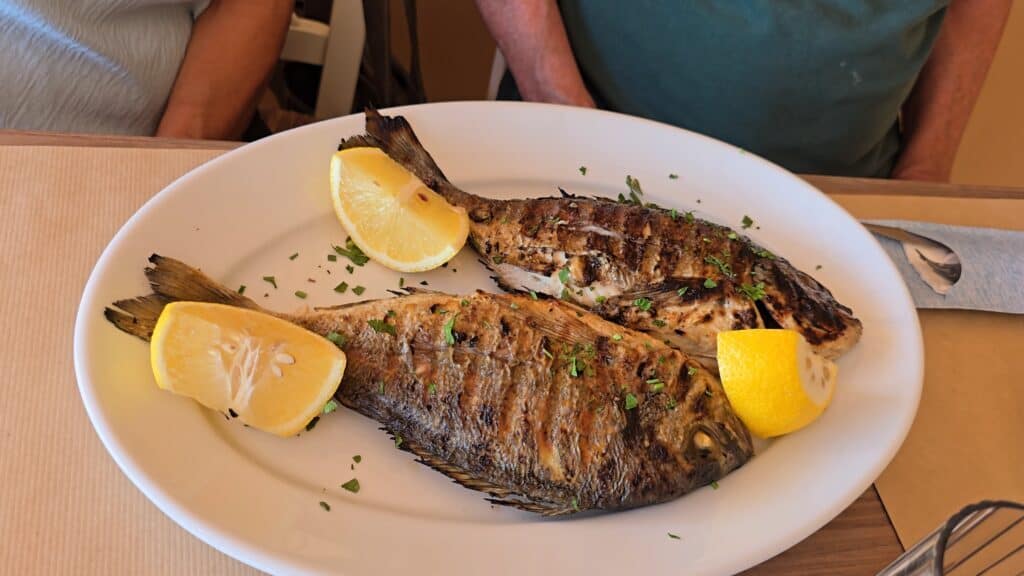 Tsambika Beach Rhodes: The Greek Flag Rock, Golden Sand & Crystal Clear Sea 5 Close-up of the main course from the Special Seafood for 2 combo: two whole grilled Sea Bream (Orata) garnished with lemon slices and herbs, demonstrating a generous portion size.