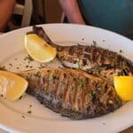Close-up of the main course from the Special Seafood for 2 combo: two whole grilled Sea Bream (Orata) garnished with lemon slices and herbs, demonstrating a generous portion size.