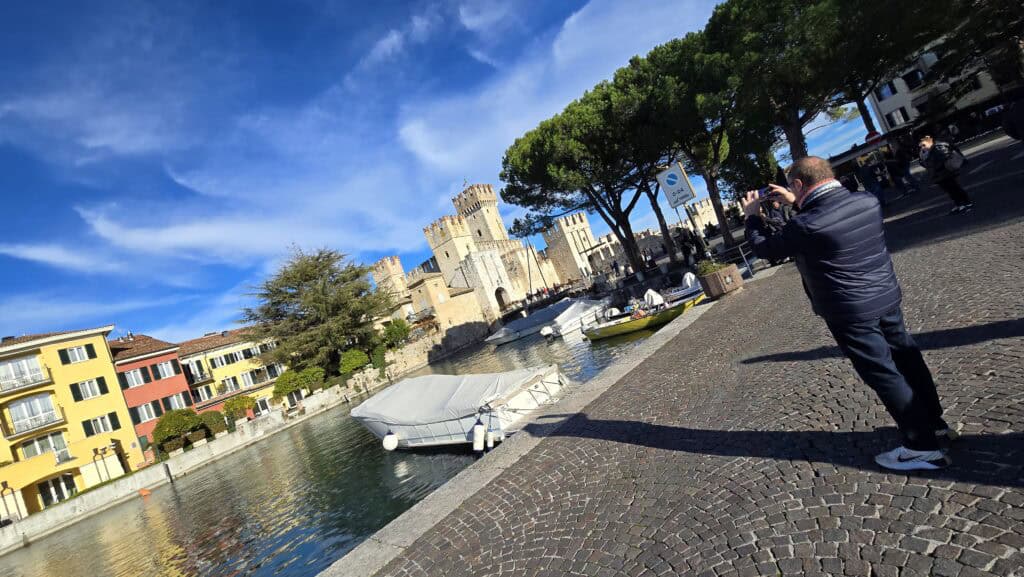 Gabriel, wearing a heavy winter jacket, takes a photo of the Scaligero Castle in Sirmione, documenting the peaceful and historic atmosphere of Lake Garda in the off-season.