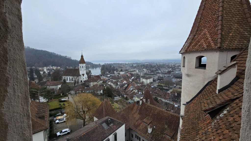A high-angle panoramic view of the city of Thun and the lake from the top of the castle tower under a grey winter sky, as seen by author Ila from Tripilare.