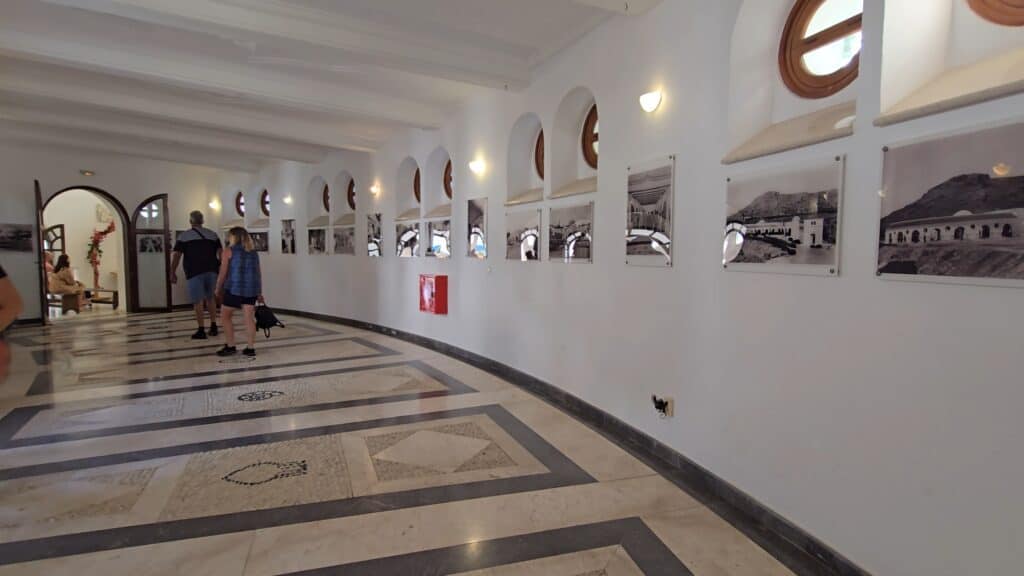 Majesty Reborn: Kallithea Springs Rhodes โ Italian Thermal Baths, Beaches & Architecture 7 Interior corridor at Kallithea Springs featuring historical black and white photographs mounted on the white wall, showcasing the architecture and people from the past era.