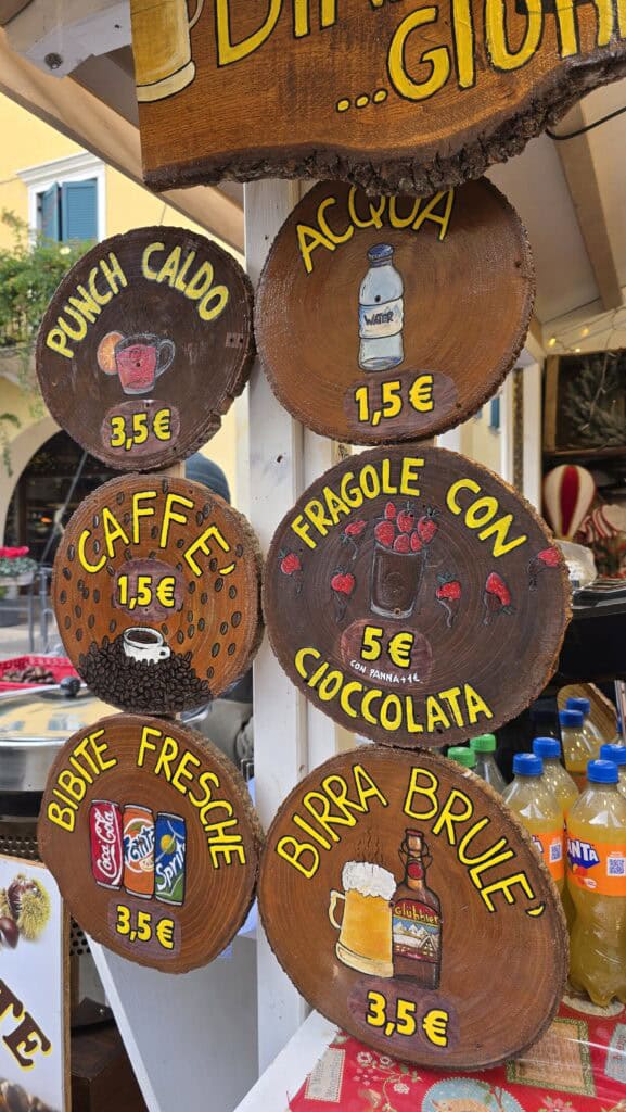 A close-up shot of a typical market snack (e.g., castagne, pretzels, or a dessert) being handed to a customer from a Lazise Christmas Market stall. The item is hot and ready to eat.