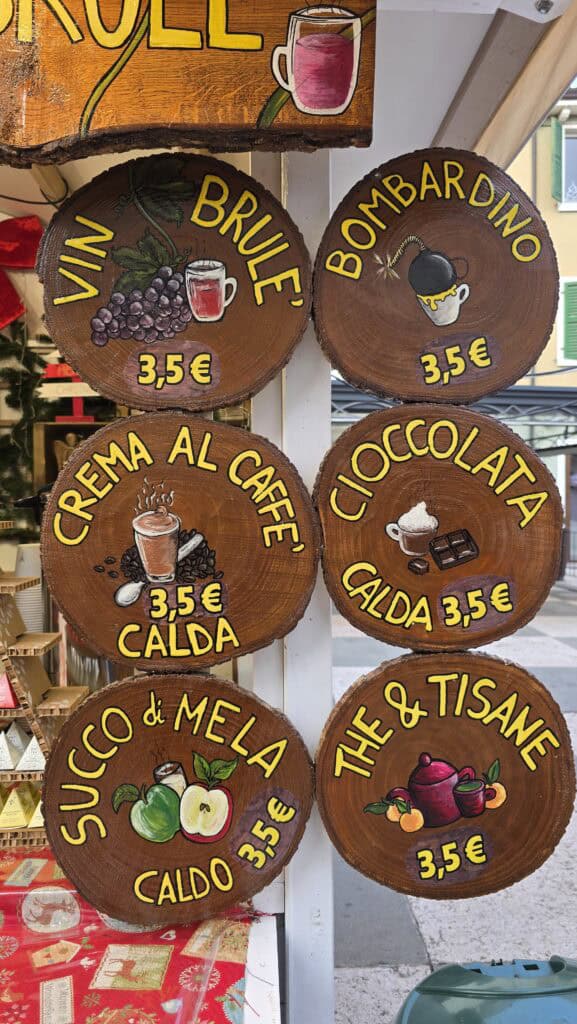 A photograph showing a market stall menu board in Lazise with clearly displayed prices in Euros (€) for food, drinks, and snacks, confirming the high level of price transparency at the market.