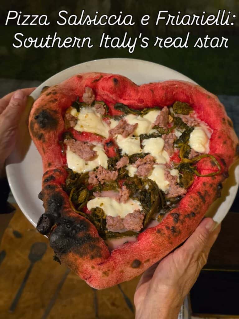 A heart-shaped red pizza with buffalo mozzarella, sausage, and friarielli, showing a slightly charred soft crust.