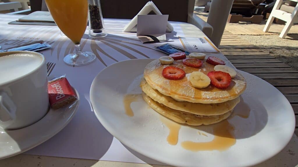 Your Guide to Paradise Mykonos: Is It a Party Beach or a Relaxing Escape? 4 A close-up of the fluffy pancakes with honey, strawberries, and bananas enjoyed by Ila, the author of tripilare.com, during her personal morning ritual at Tropicana, Paradise Beach, Mykonos.