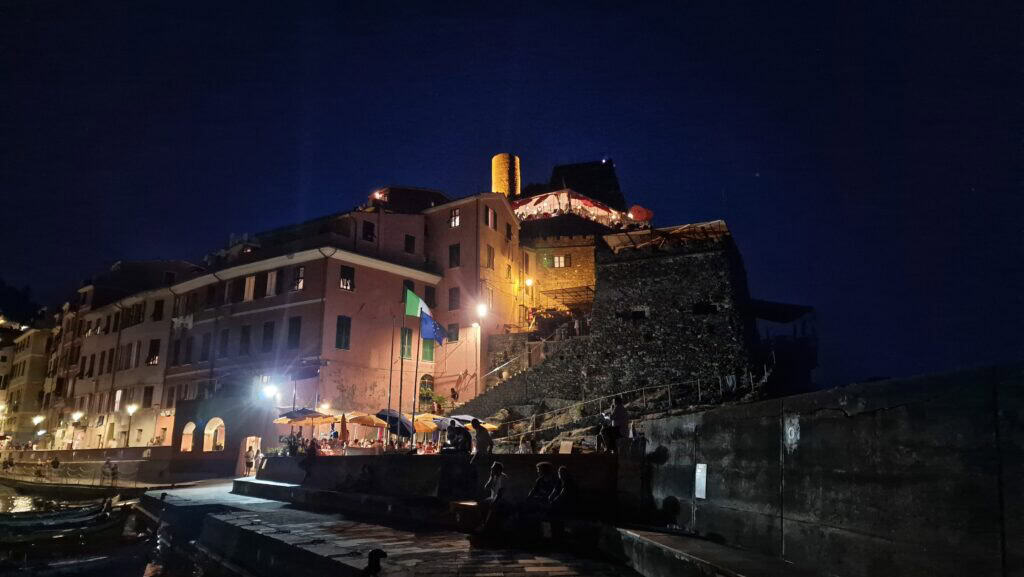 Vernazza Italy: A Gem of the Cinque Terre 11 View of Vernazza harbor at night with illuminated restaurant terraces and the glowing tower of Doria Castle against a dark sky.