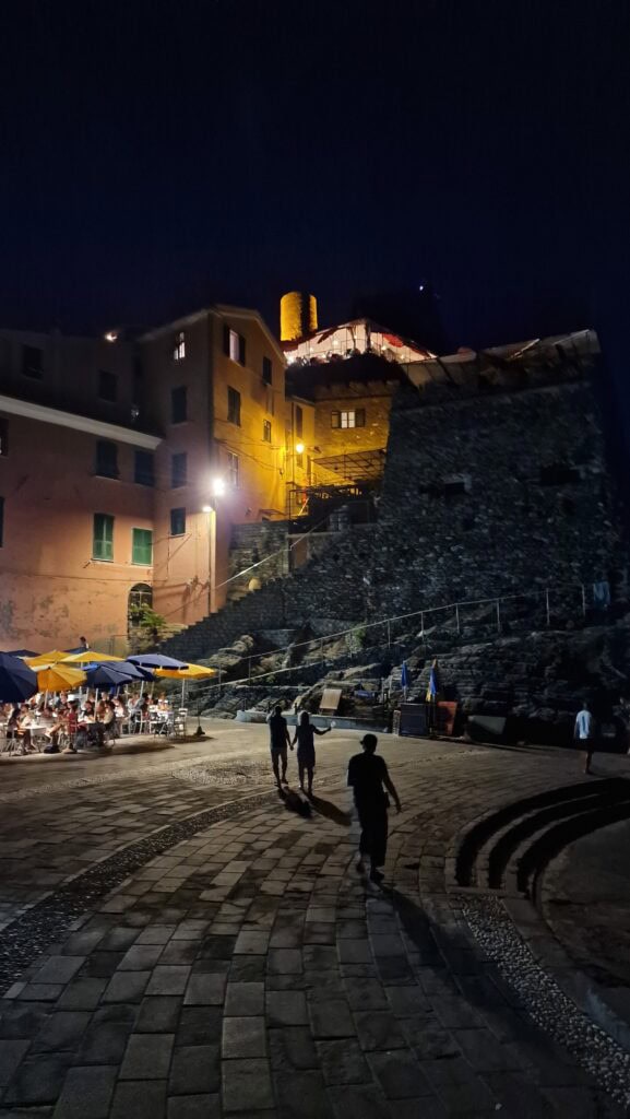 Vernazza Italy: A Gem of the Cinque Terre 12 Vernazza's main square and harbor at night in August, showing quiet stone streets and illuminated restaurant terraces filled with people.