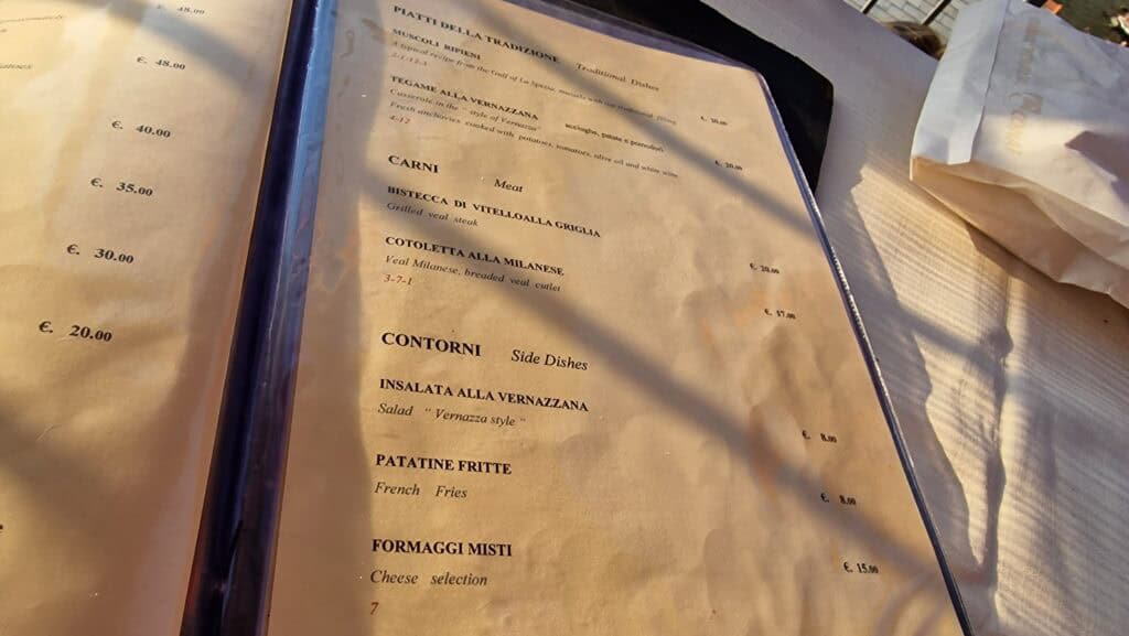 Vernazza Italy: A Gem of the Cinque Terre 9 Close-up of a restaurant menu in Vernazza showing traditional Ligurian dishes and prices from August 2023, including Tegame alla Vernazzana and seafood specialties.