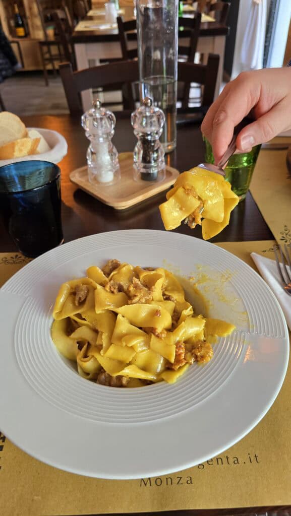 Monza: The Royal Escape Just a Stone's Throw from Milan 3 A forkful of golden pappardelle pasta with sausage held over a white plate in a restaurant in Monza.