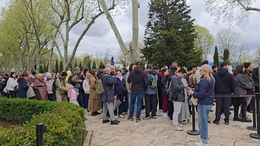 A massive, packed crowd of tourists waiting in a long, unorganized line at Topkapi Palace courtyard in Istanbul during the afternoon of May 1st, 2026.