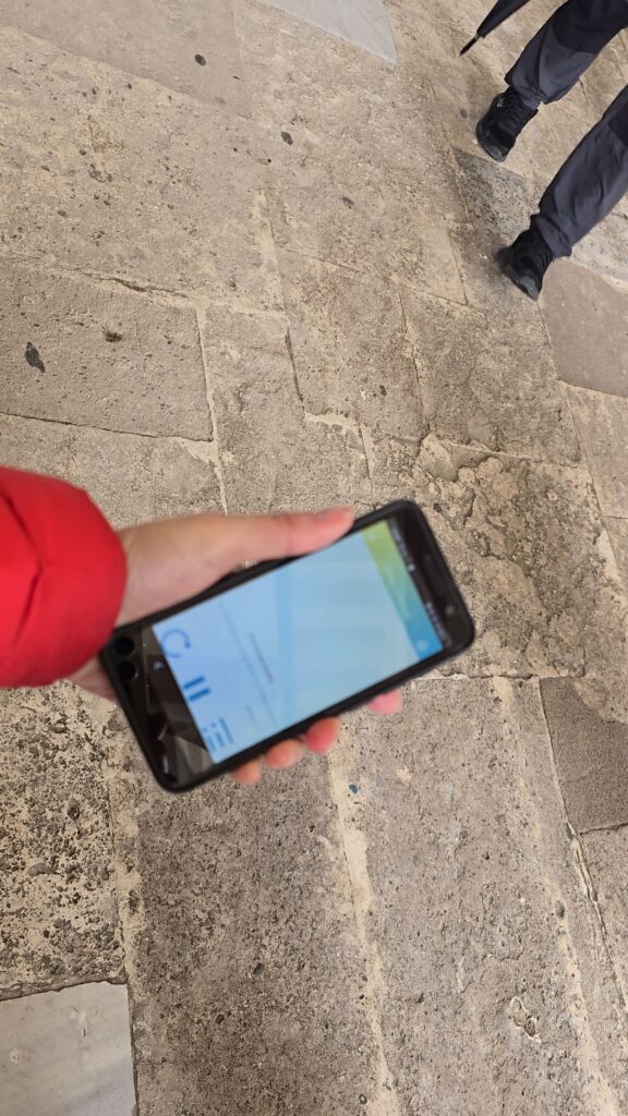 Ila, the author, holding the official handheld audioguide device provided at Topkapi Palace entrance in Istanbul, showing the screen interface.