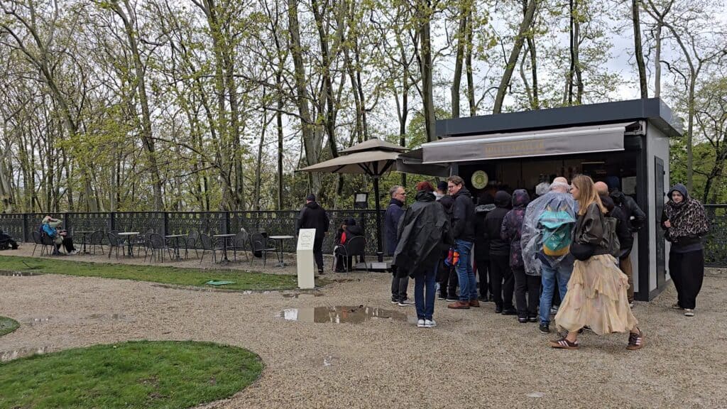 Tourists crowded under the small awning of an outdoor cafe kiosk at Topkapi Palace in Istanbul on a rainy, overcast day.