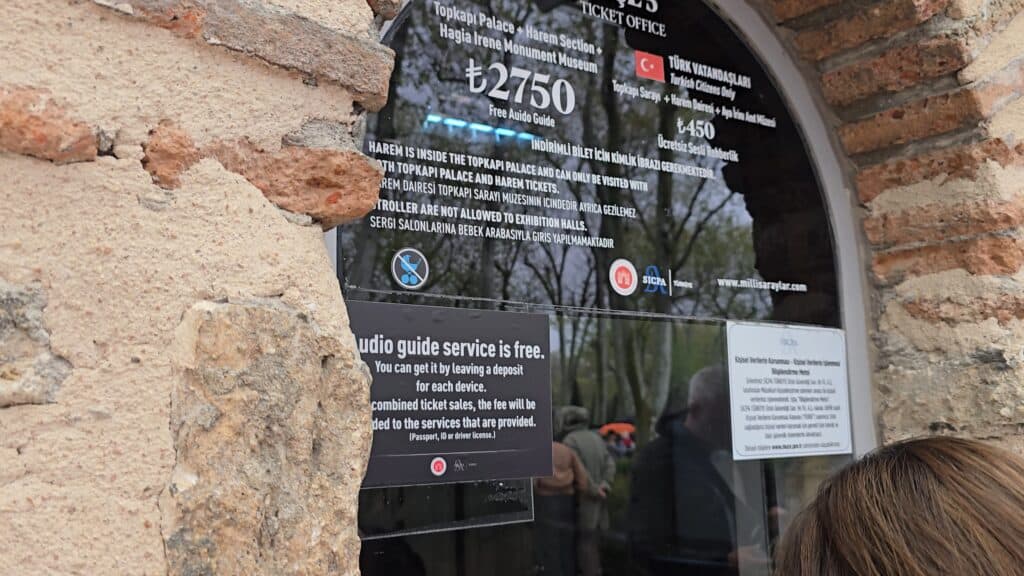Close-up of the official ticket office window sign at Topkapi Palace in Istanbul showing admission prices, Harem section info, and the free audioguide notice on May 1st, 2026.