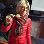 Ila smiling while holding a customized piece of torrone on a wooden stick, standing in Cremona's Piazza Duomo area during the Torrone Festival.