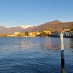 Panoramic view of Lake Iseo's waterfront in autumn, showing the colorful houses, port, and surrounding mountains with fall foliage in Iseo town, Italy.
