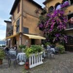 Outdoor café in a charming Monte Isola village, featuring vibrant purple bougainvillea and cobblestones, illustrating the relaxed dining atmosphere on Lake Iseo in October.