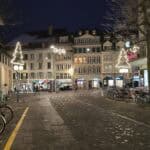 Thun city center square at night with Christmas lights and shops open, a perfect stop for shopping on the Green Train itinerary.