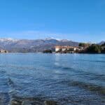 Wide panoramic view of the Borromean Islands (Isola Bella and Isola Pescatori) and the majestic snow-capped Alps mountains across Lake Maggiore in spring.