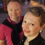 A couple smiling in front of a Minigolf sign on the promenade in Playa de Las Américas, Tenerife, at dusk.