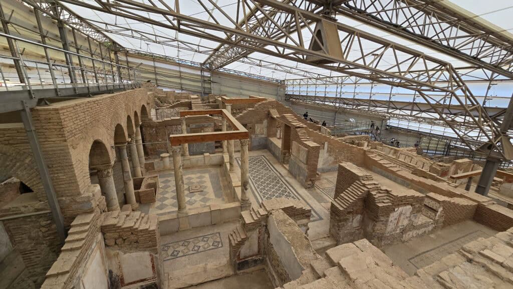 Ephesus & Kusadasi: A Sanctuary of History and the Soul of the Aegean 3 Wide angle view of the Roman Terrace Houses in Ephesus under a protective metal roof structure, featuring ancient brick walls, mosaic floors, and tourist walkways.