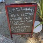 Signboard at a Cisano lakeside kiosk detailing sunbed, umbrella, and table rental prices.