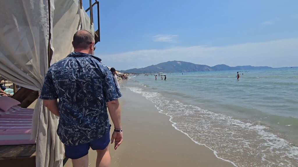 Gabriel walking on Laganas Beach during the day in Zakynthos Greece showing the murky brownish water