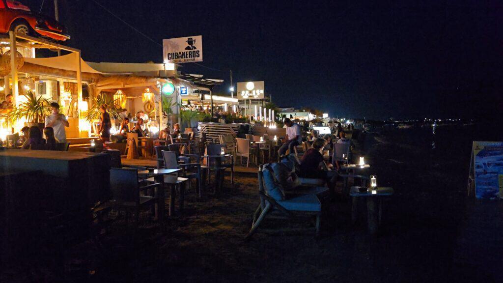 Vibrant beach bars lit up at night on Laganas Beach in Zakynthos Greece with tables on the sand